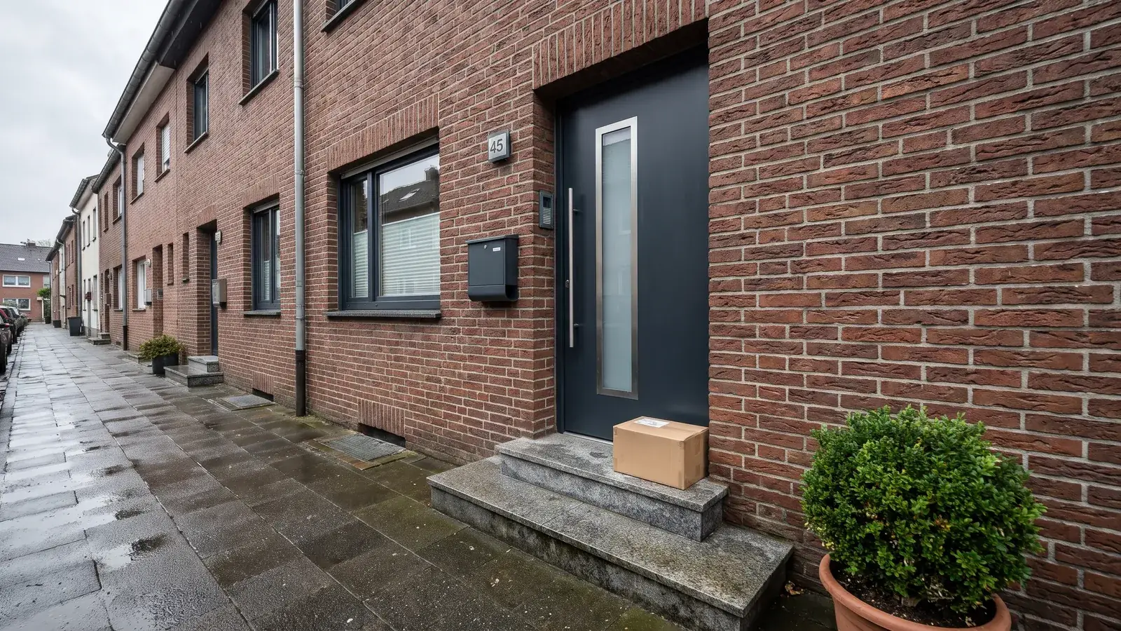 Karton auf der Stufe vor einer Haustür, daneben ein Briefkasten an der Hauswand